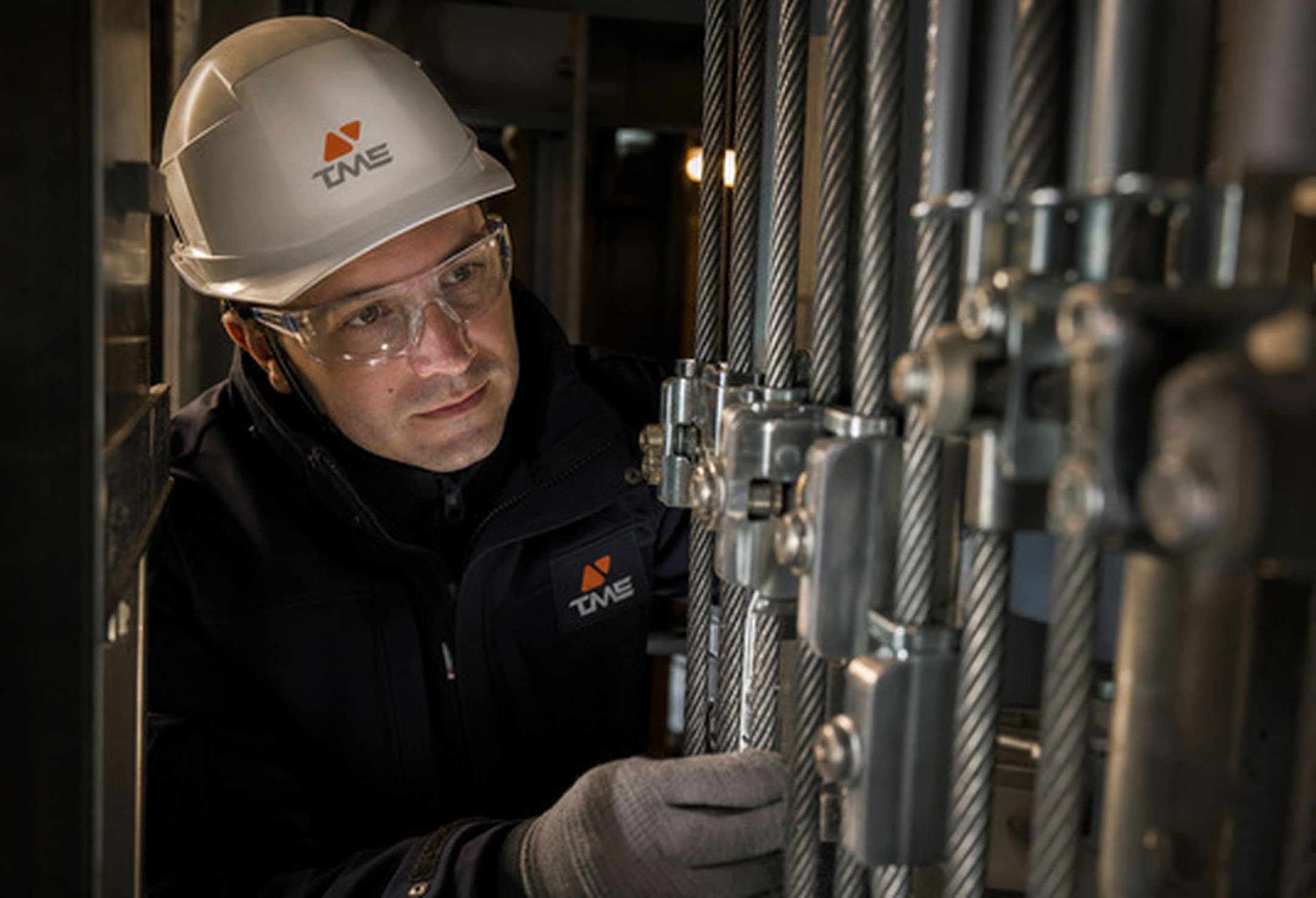 Technicien TME inspectant les câbles de traction d'un ascenseur